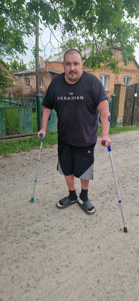 Олексій стоїть на милицях біля свого будинку